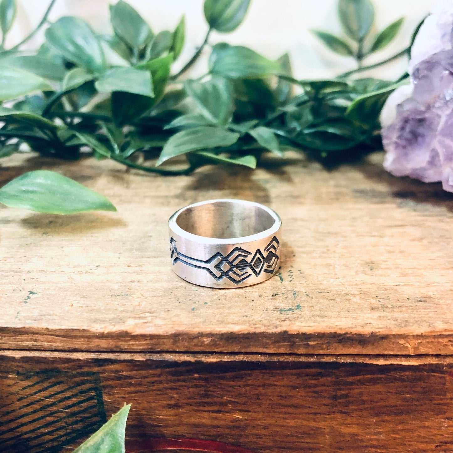 Vintage silver band ring with geometric tribal design on wooden surface with plants in background