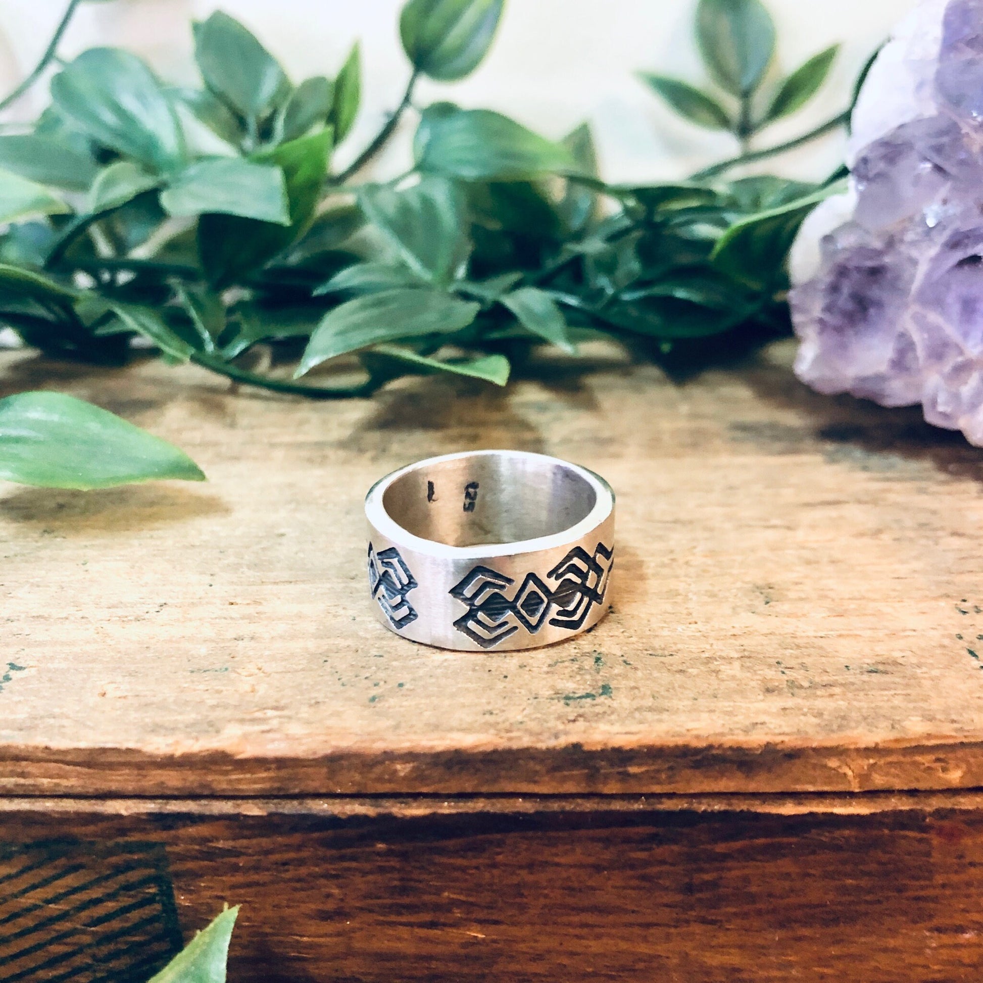 Vintage silver geometric tribal design band ring on wooden surface with greenery and amethyst crystal in background