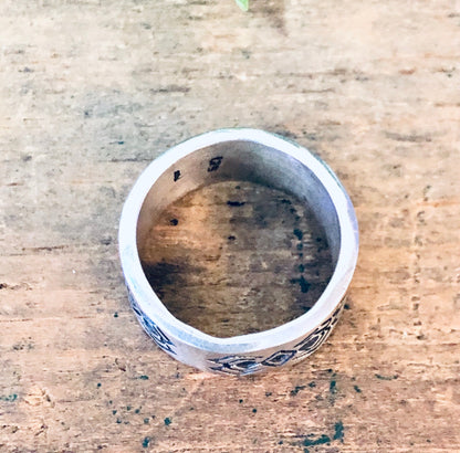 Vintage silver band ring with geometric tribal design on rustic wood surface