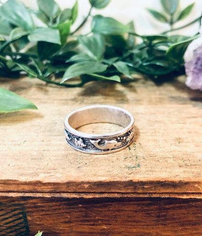 Vintage silver aquatic dolphin and sun ring on wooden surface with greenery in background