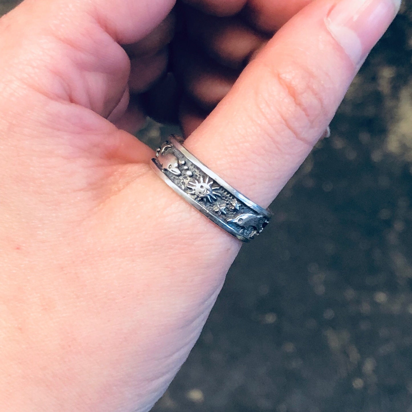 Vintage silver aquatic ring with dolphin and sun design, worn on thumb as a skinny band ring