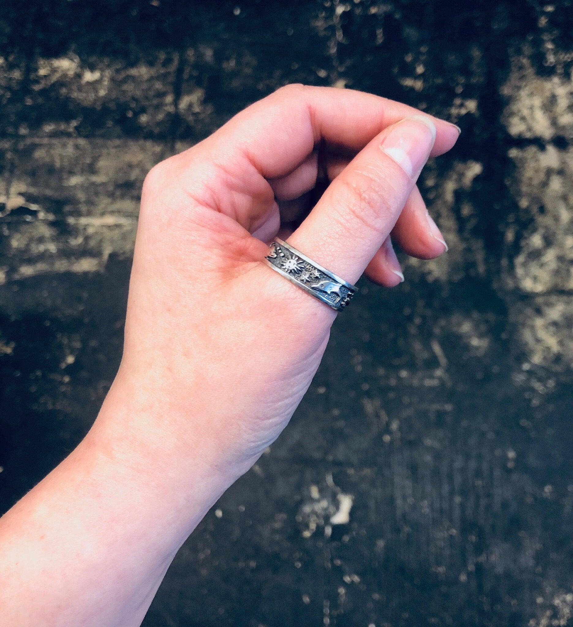 Vintage silver dolphin ring worn on thumb against weathered wooden background