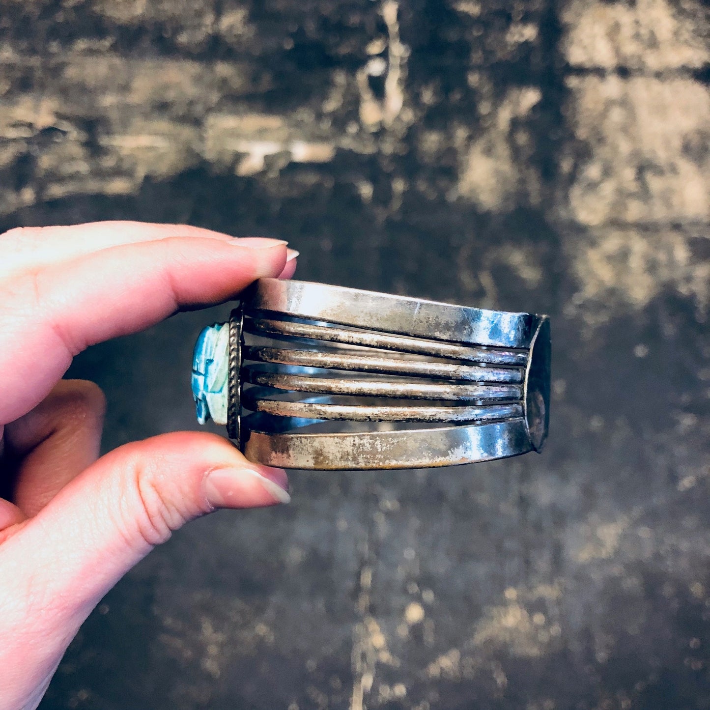 Vintage silver-toned cuff bracelet with blue scarab design, held in hand against textured background