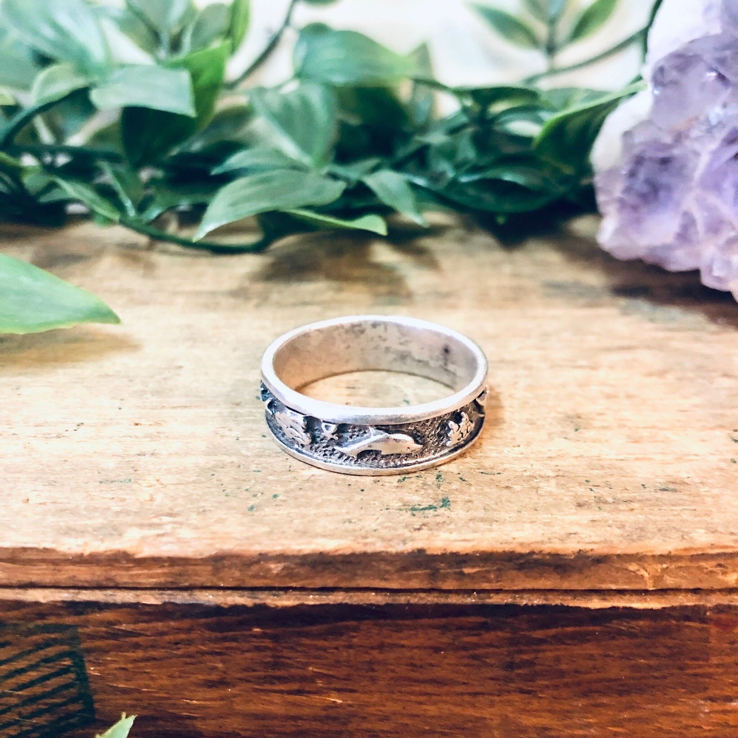 Vintage silver dolphin and sun design band ring on wooden surface with greenery in background