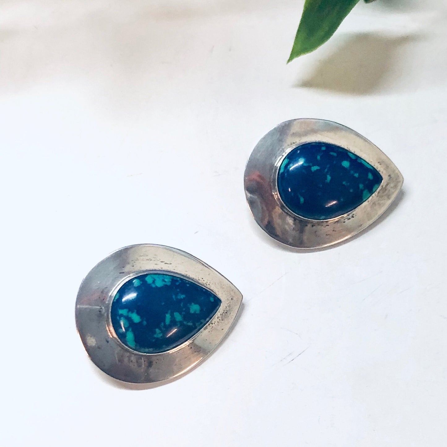 Vintage silver clip-on earrings with teardrop-shaped azurite malachite stones in deep blue and green hues, displayed on a white background with a green leaf.