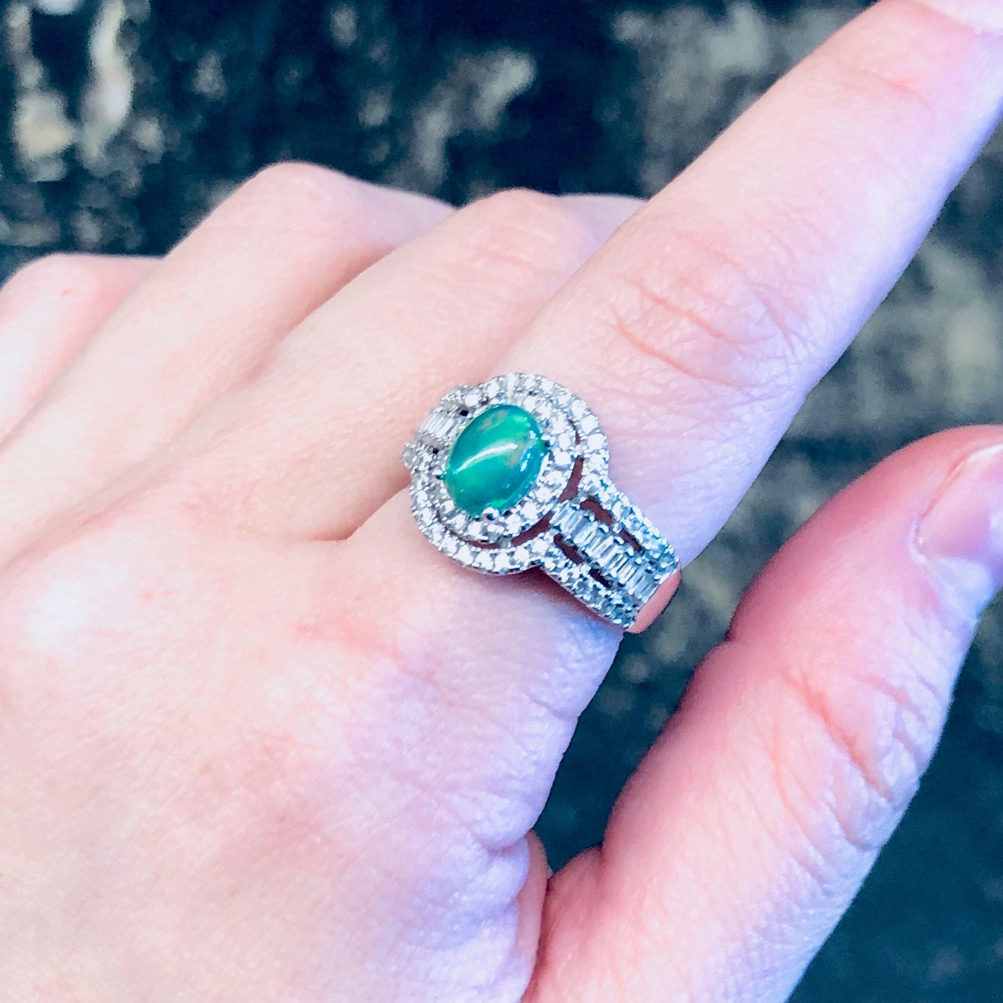 Vintage silver ring with green center stone surrounded by clear faux diamonds, worn on finger