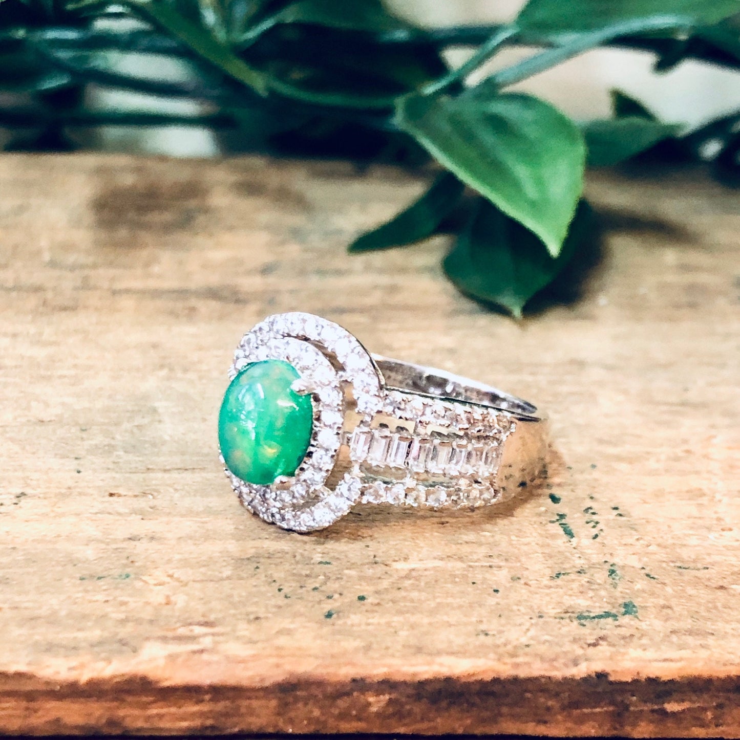 Vintage silver ring with green opalescent stone and faux diamonds, statement jewelry piece on rustic wooden surface with greenery in background