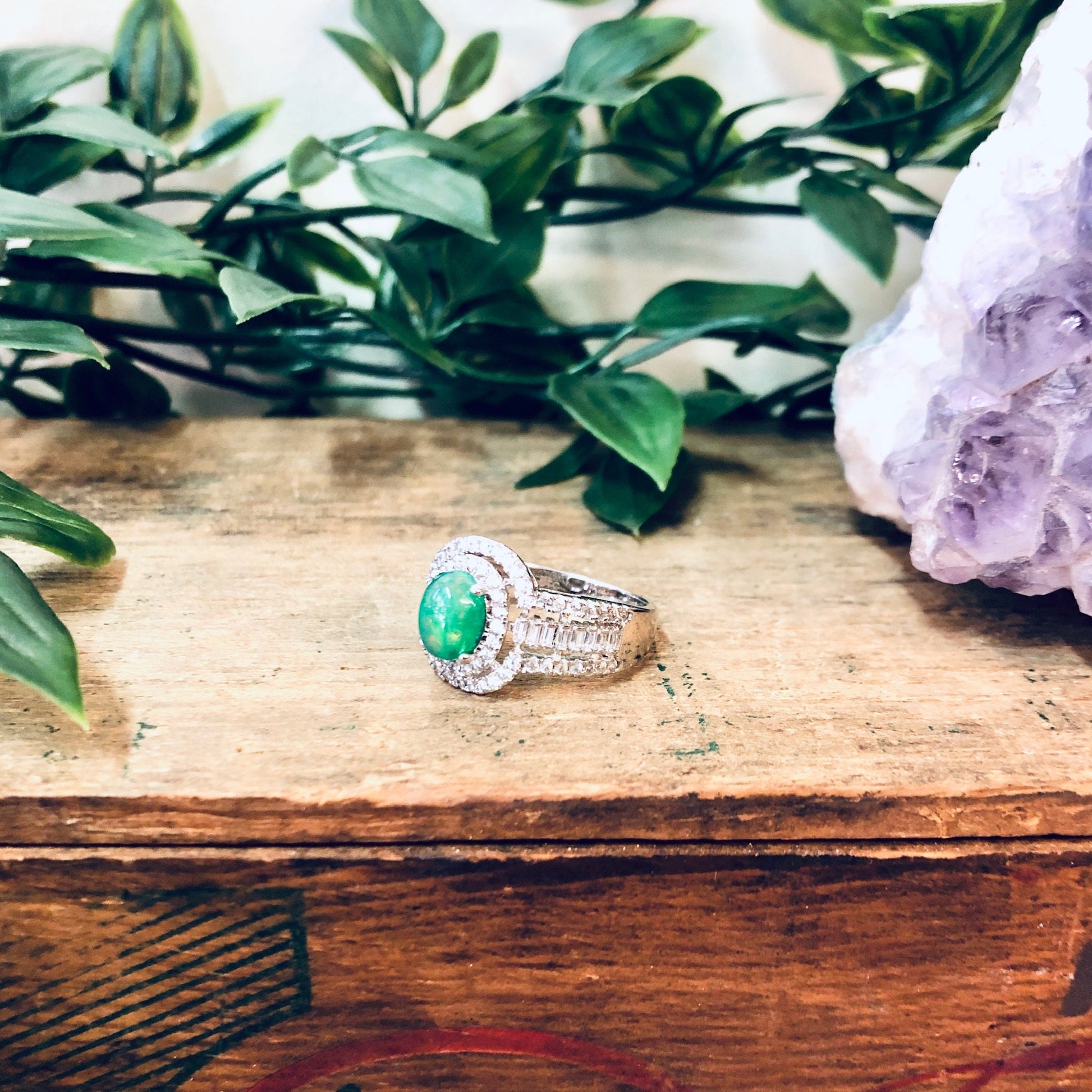 Vintage silver ring with green and opalescent stones on wooden surface surrounded by greenery