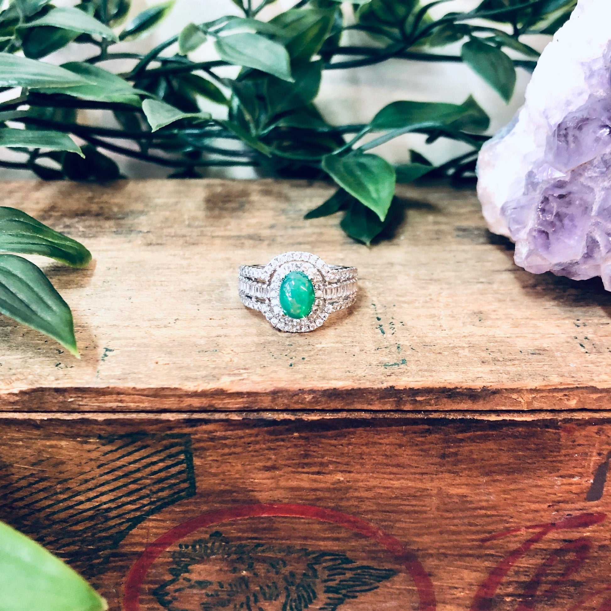 Vintage silver ring with green and opalescent stones on wooden surface with greenery