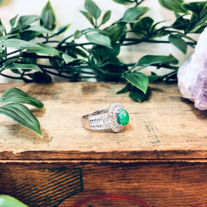 Vintage silver ring with green and opalescent stones on rustic wooden surface surrounded by lush greenery