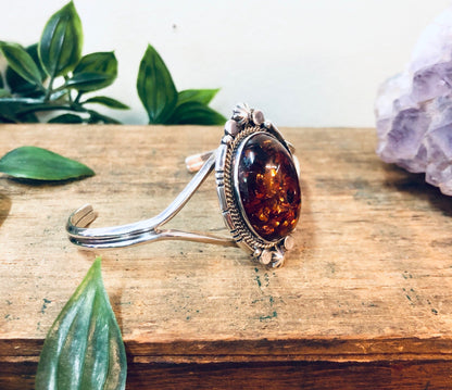 Vintage amber gemstone cuff bracelet in silver setting on wooden surface with crystal and greenery accents, perfect Valentine's Day or anniversary gift for wife or girlfriend.