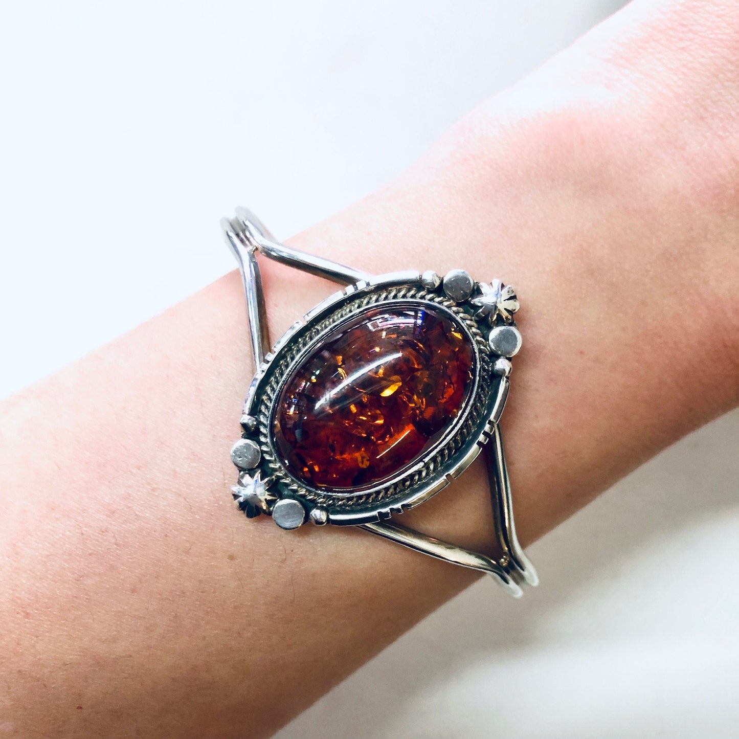 Vintage amber gemstone cuff bracelet with ornate silver setting on wrist, orange glowing stone, artisan jewelry gift