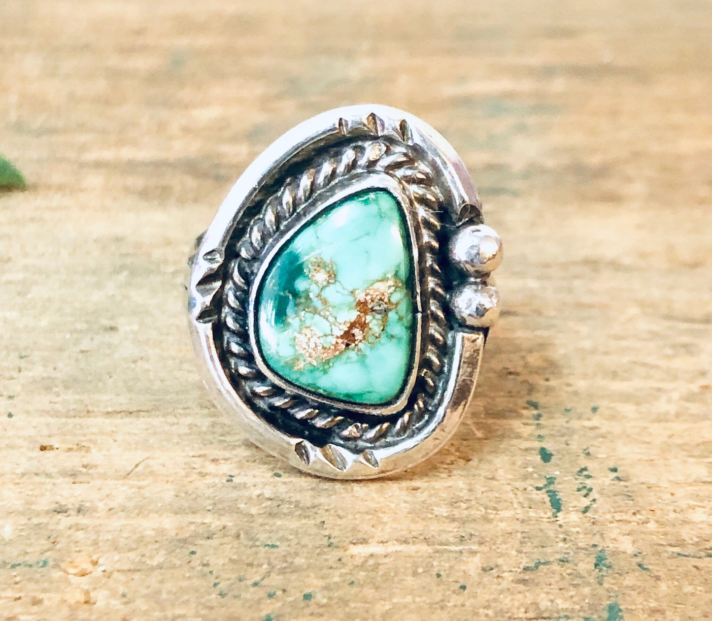 Vintage silver ring with green turquoise stone and bohemian style rope detailing, displayed on a wooden surface.