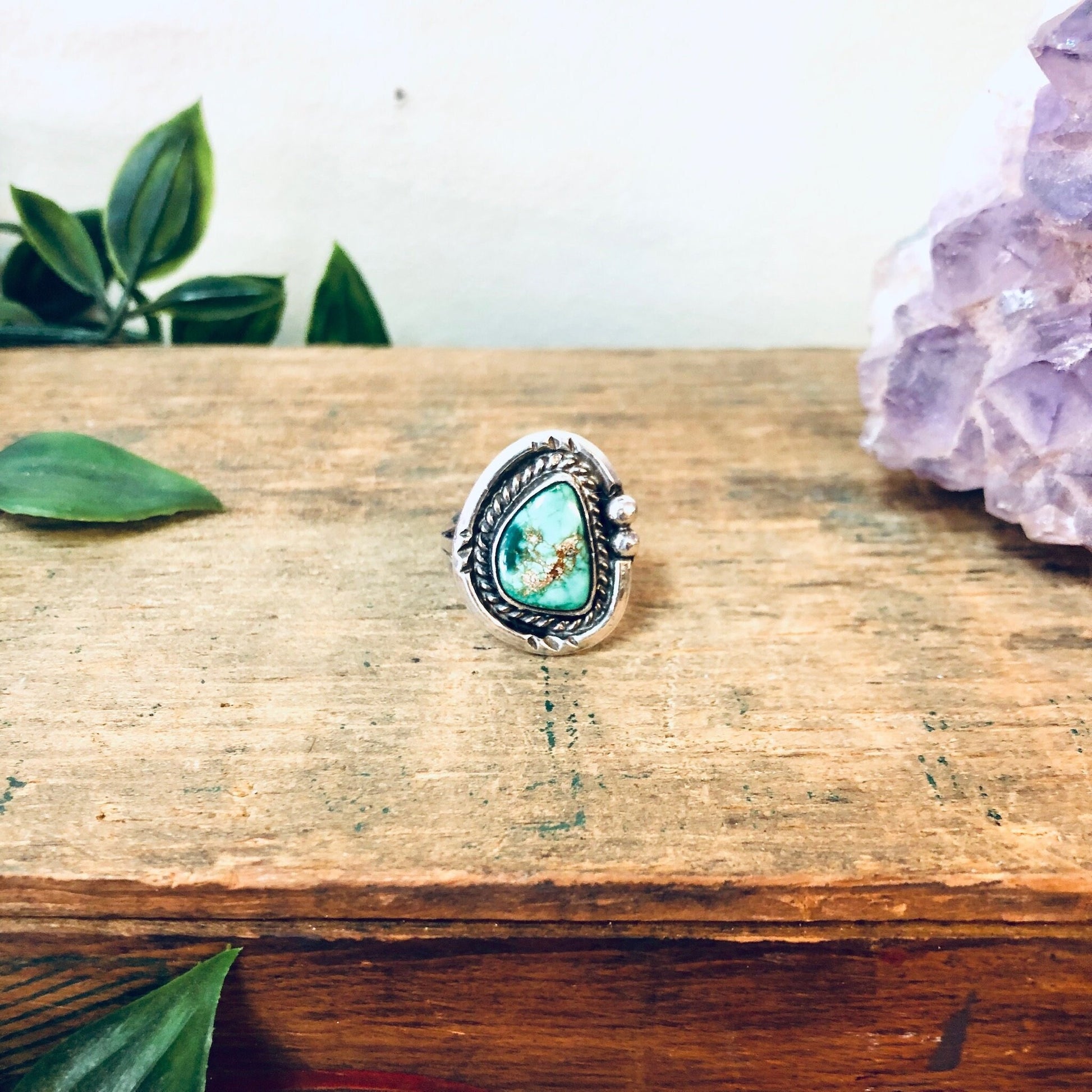 Vintage turquoise and silver ring on wooden surface with amethyst crystal and green leaves