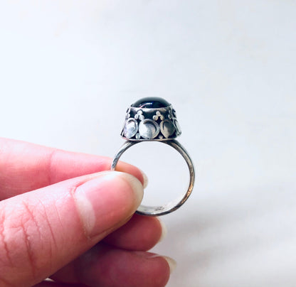 Vintage silver ring with black onyx stone cabochon, crafted in decorative bezel setting, held between fingers against white background