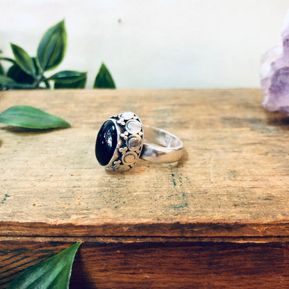 Vintage silver and black onyx statement ring on wooden surface with green leaves