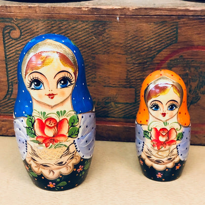 Two colorful Russian nesting dolls showing floral designs and female faces, made of painted wood, resting on a wooden surface with a decorative background.