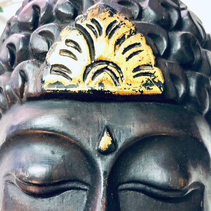 Vintage wood carved mask with dark brown finish and gold accents, depicting closed eyes and arched eyebrows, used as wall decor or Asian art piece in vintage home decor.