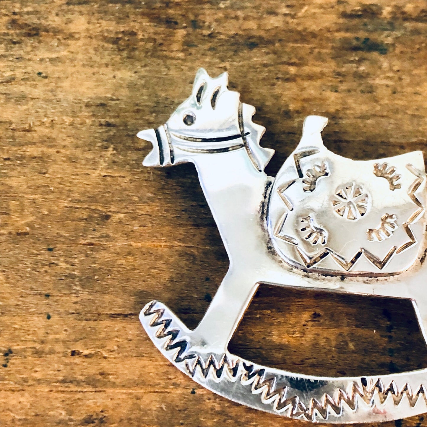 Vintage silver rocking horse brooch pin with ornate details, made in Mexico and stamped 925, displayed on a rustic wooden surface.