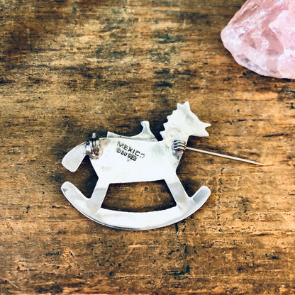 Vintage silver rocking horse brooch pin from Mexico, 925 sterling silver, on rustic wooden surface with pink quartz crystal, suitable as Valentine's Day gift or horse lover jewelry.