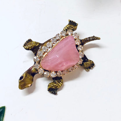 Vintage gold-toned turtle brooch with pink gemstone shell, rhinestone accents, and textured body, an eye-catching piece of animal-themed jewelry from the past.