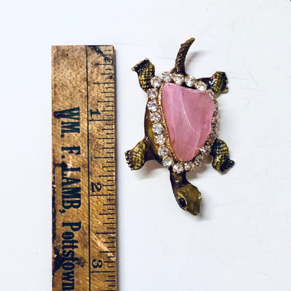 Vintage gold-toned turtle brooch pin with pink gemstone shell and rhinestone accents, measuring against antique wooden ruler.