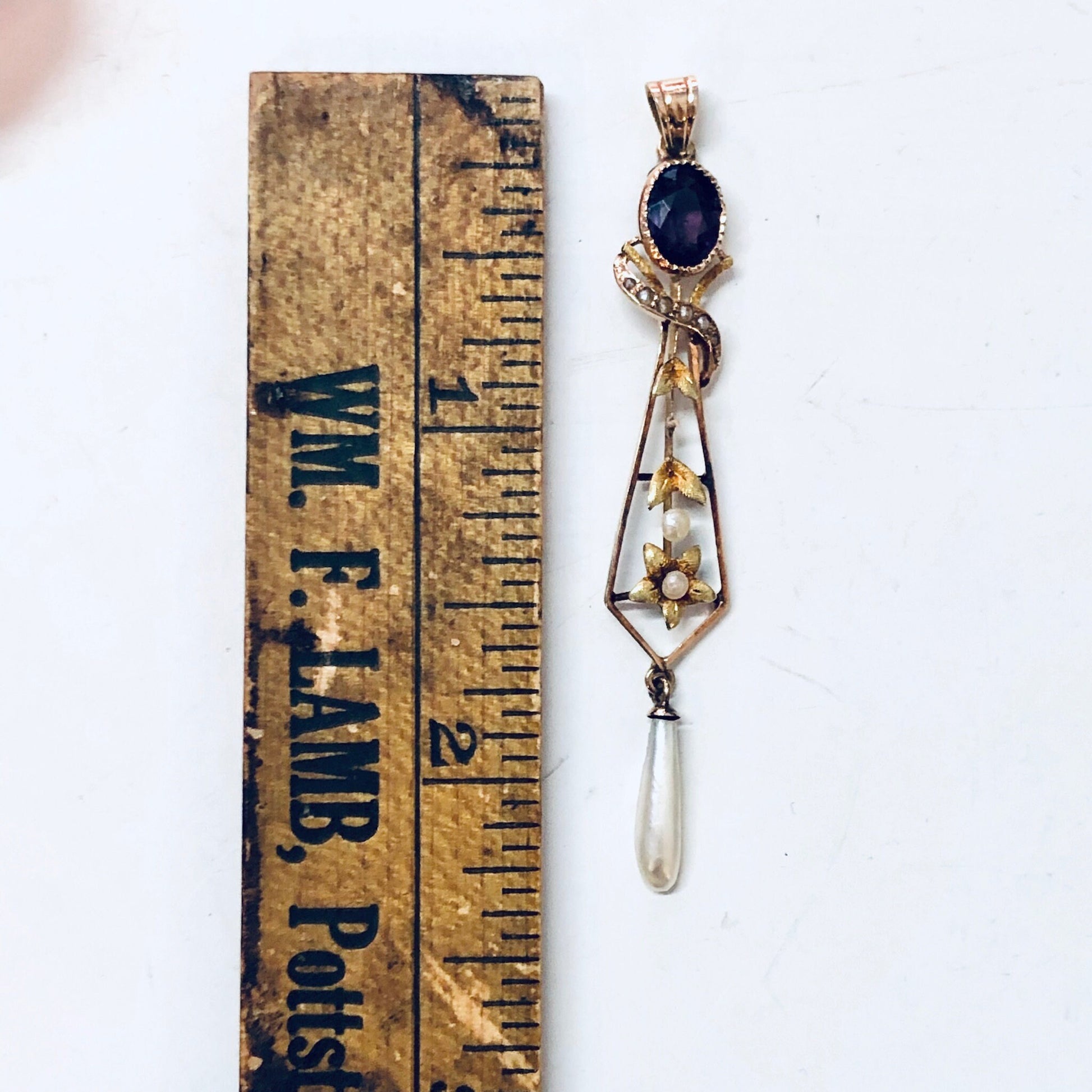 Vintage 14K yellow gold pendant necklace with amethyst stone, pearl drop, and floral design, shown next to antique ruler for scale.