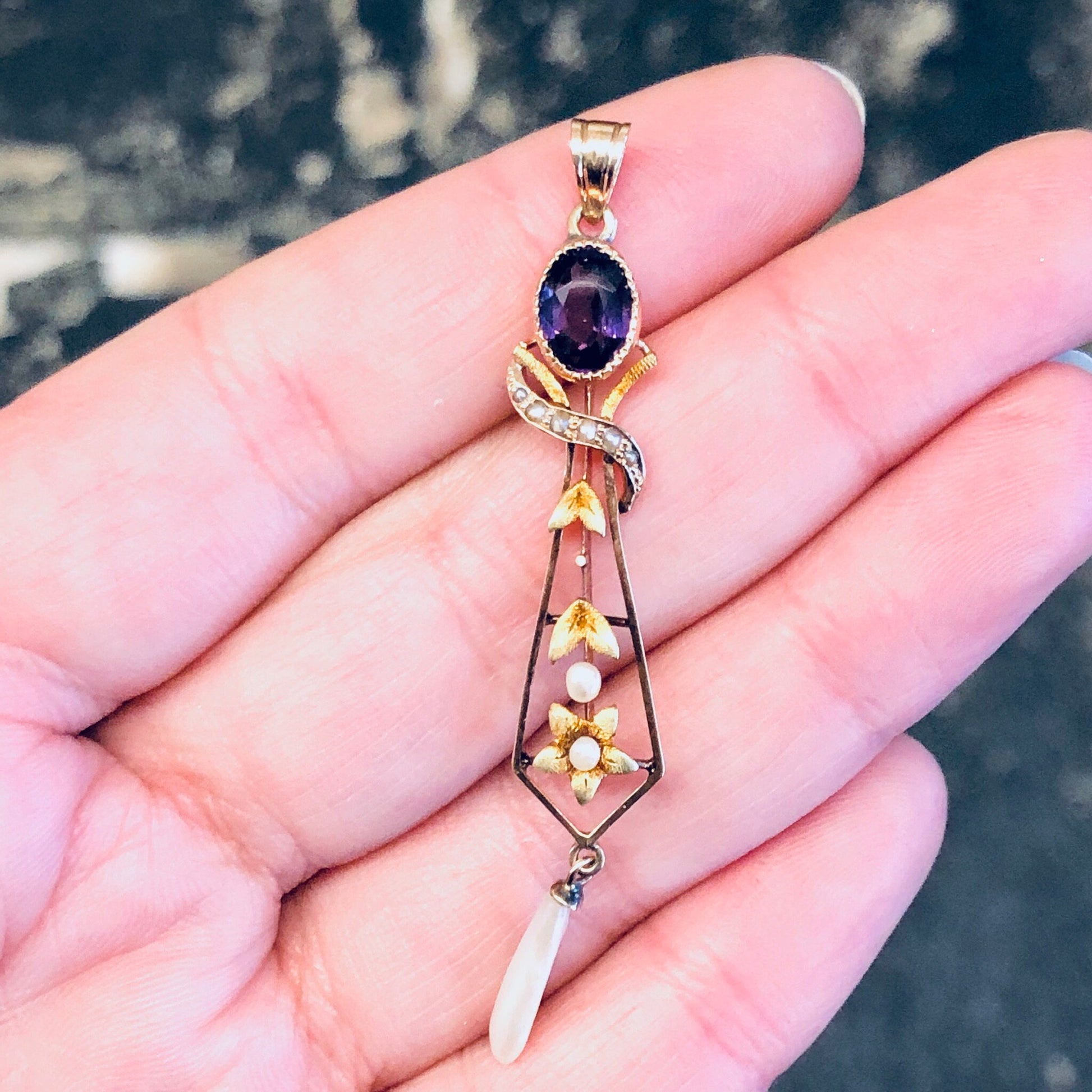 Vintage 14K yellow gold pendant necklace with amethyst stone, pearl accents and floral design, held in palm of hand