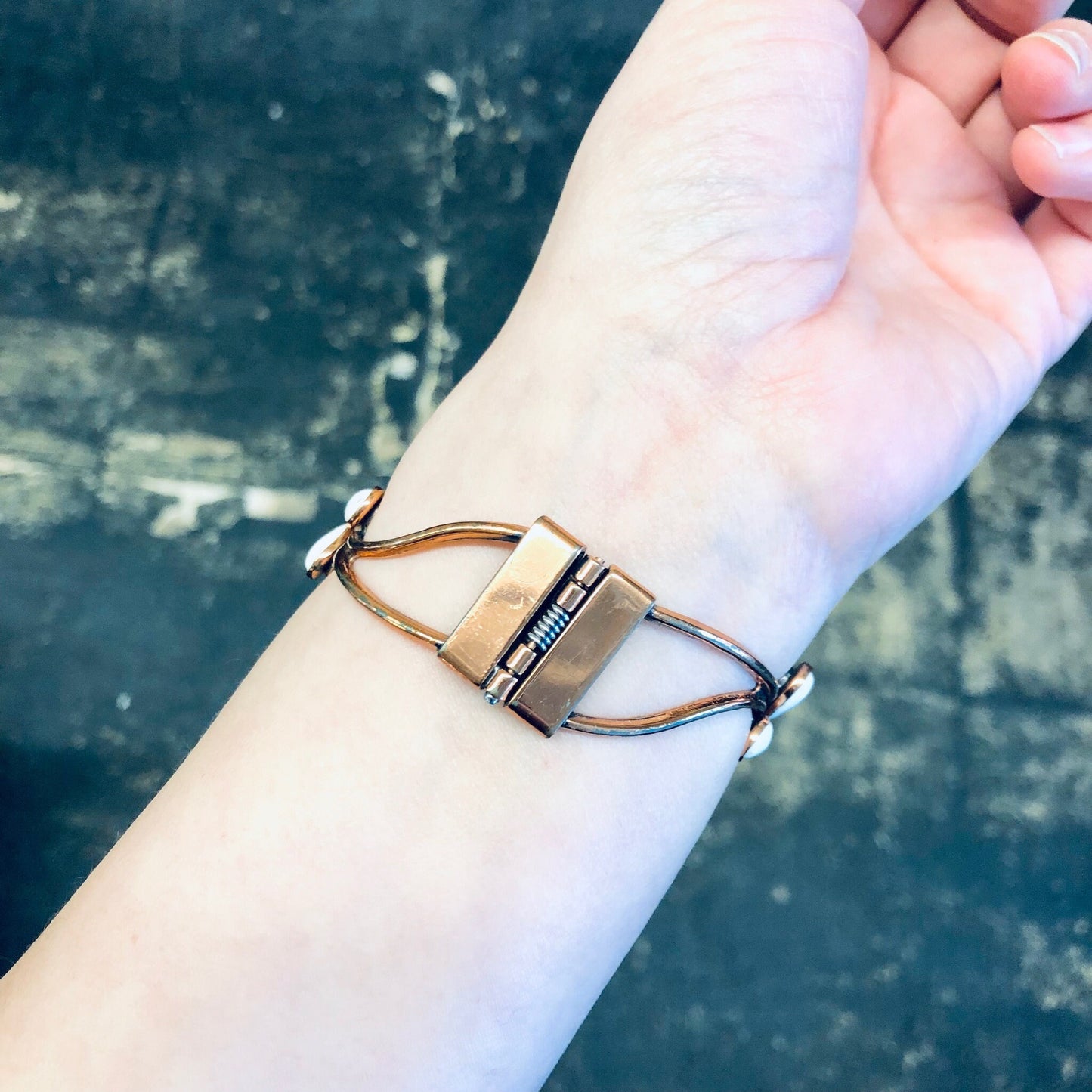 A hand wearing a vintage copper Matisse bracelet and brooch set with white enamel against a grunge background.