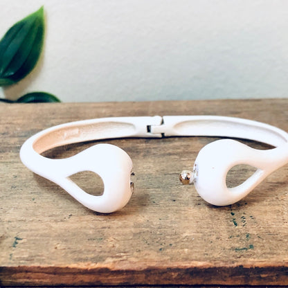 White cut out bangle bracelet on wooden surface with green leaf in background