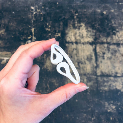 Hand holding a white cut-out bangle bracelet against a grunge textured dark background