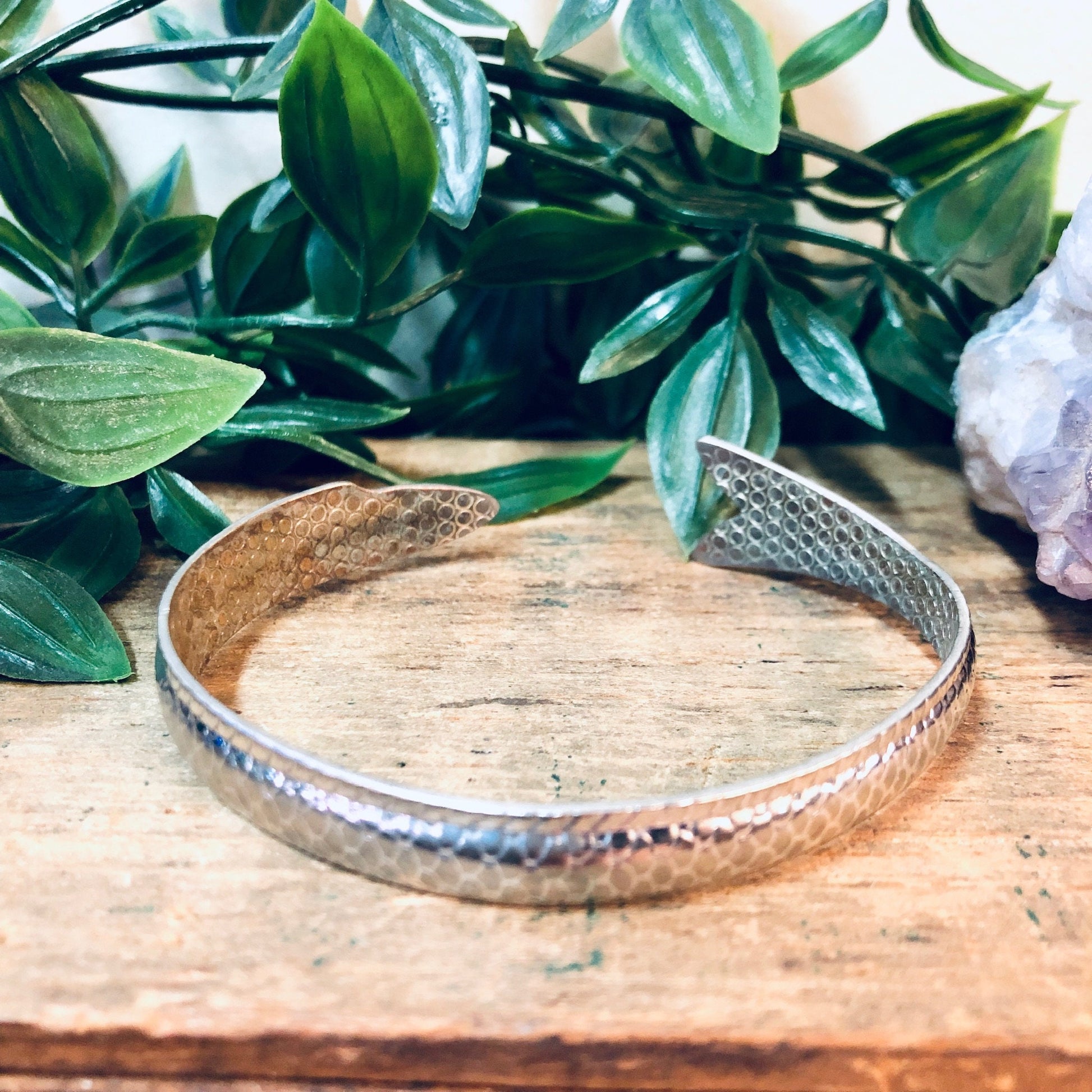 Vintage silver fish bangle bracelet on wooden surface with green leaves