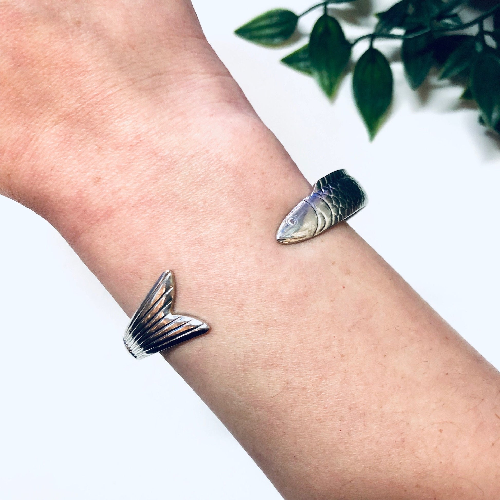 Vintage silver fish bangle cuff bracelet on wrist with plant leaves in background