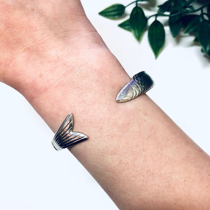 Vintage silver fish bangle cuff bracelet on wrist with plant leaves in background