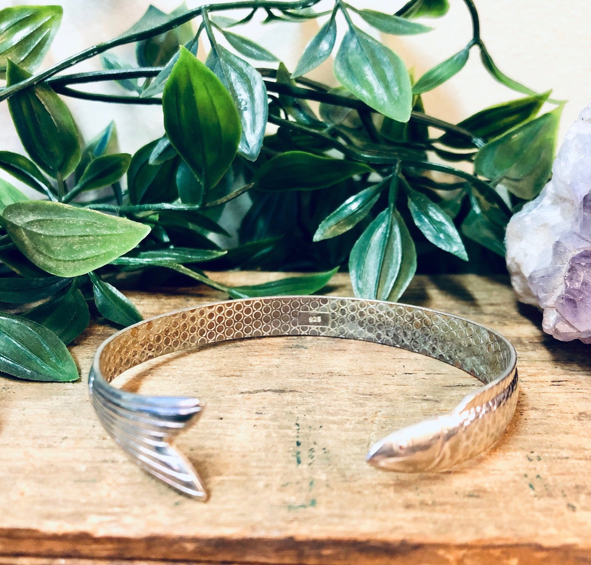 Vintage silver fish bangle bracelet on wooden surface with green leaves and amethyst crystal in background, unique aquatic animal jewelry cuff