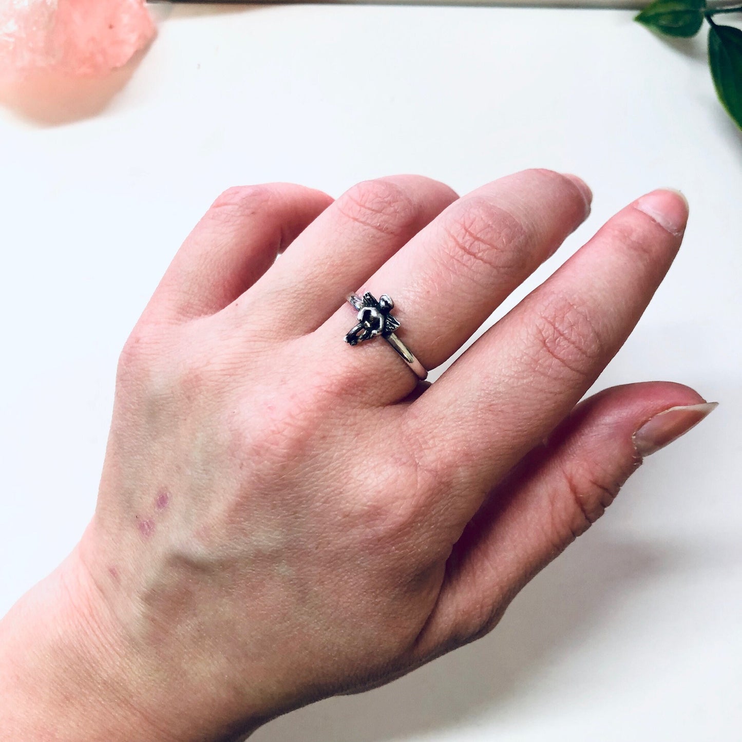 Vintage silver cherub angel ring displayed on a hand, with a rose quartz crystal and greenery in the background.