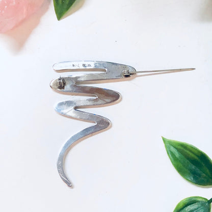 Vintage sterling silver abstract squiggle brooch pin, minimalist line design jewelry for Valentines Day or everyday wear, displayed with pink rose and green leaves on white background.