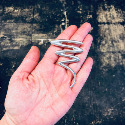 Sterling silver abstract squiggle brooch pin held in an open palm, vintage jewelry design resembling curved lines against a dark textured background.