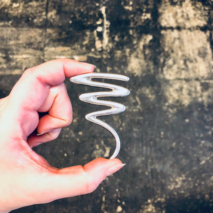 Hand holding a sterling silver vintage brooch with an abstract squiggle design, against a weathered concrete background.