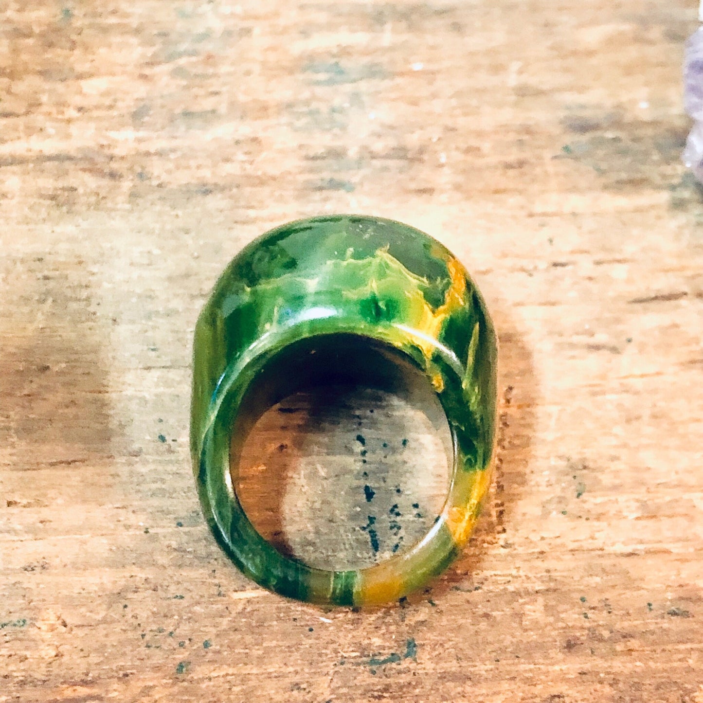 Green and yellow marbled plastic ring, round retro vintage statement jewelry piece on wooden surface, suitable as Valentine's Day gift.