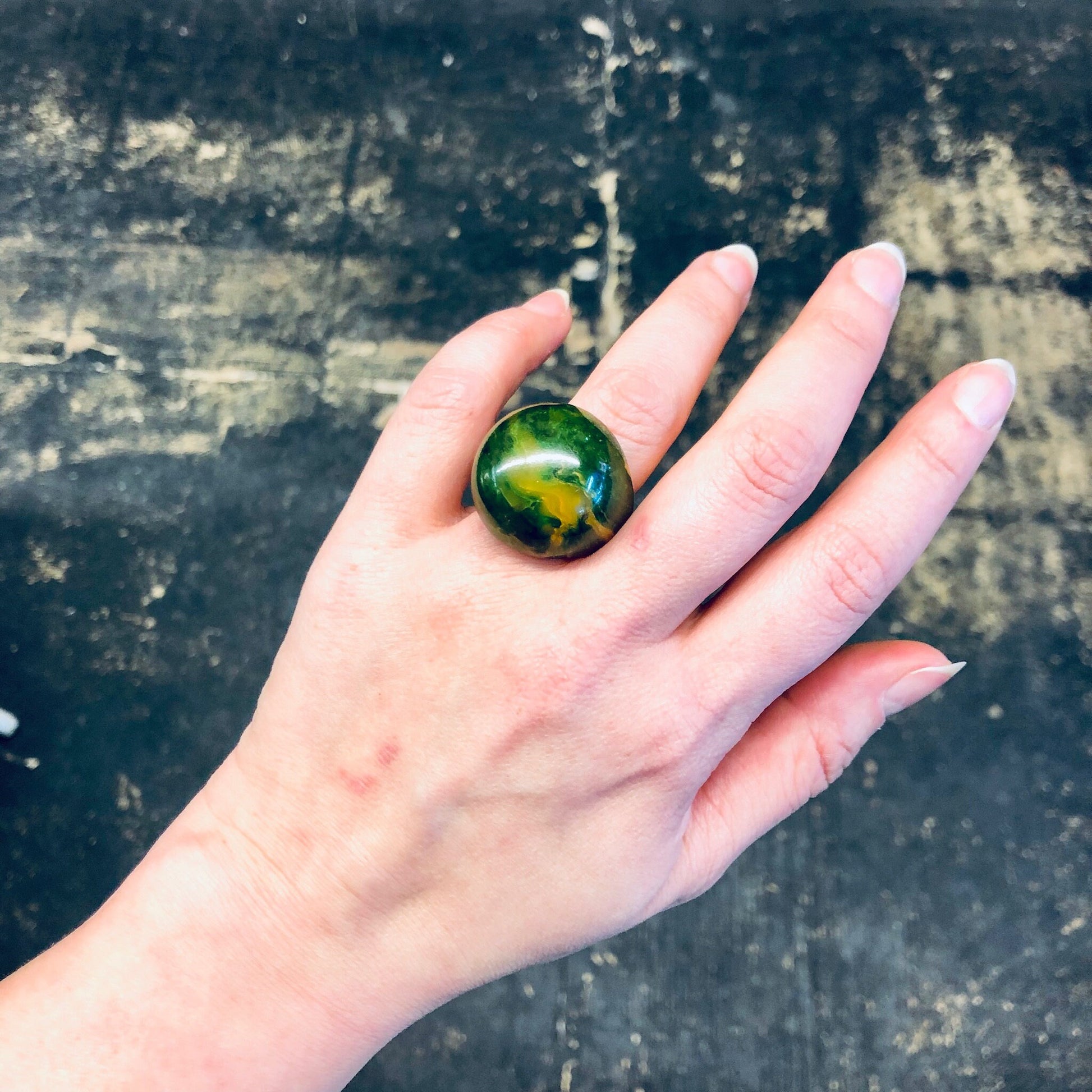 Green and yellow swirled plastic ball ring on hand against weathered concrete background