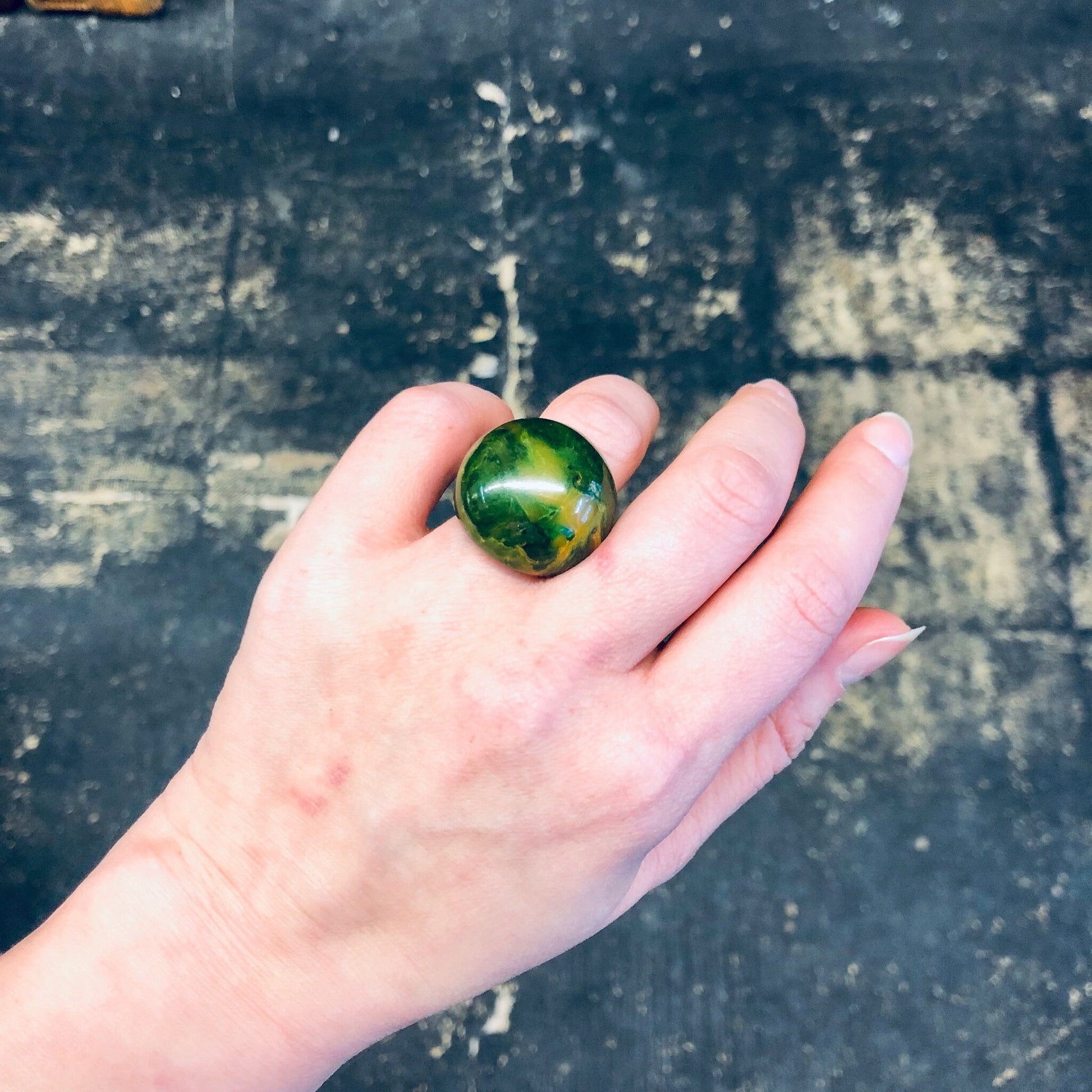 Green and yellow marble-patterned plastic ring held in a person's hand against a weathered concrete surface.