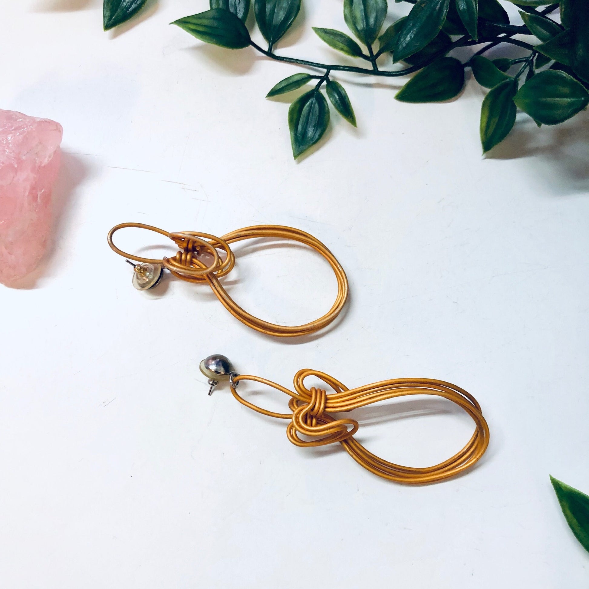 Vintage gold wire dangle earrings with abstract knot design on white background with rose quartz and greenery