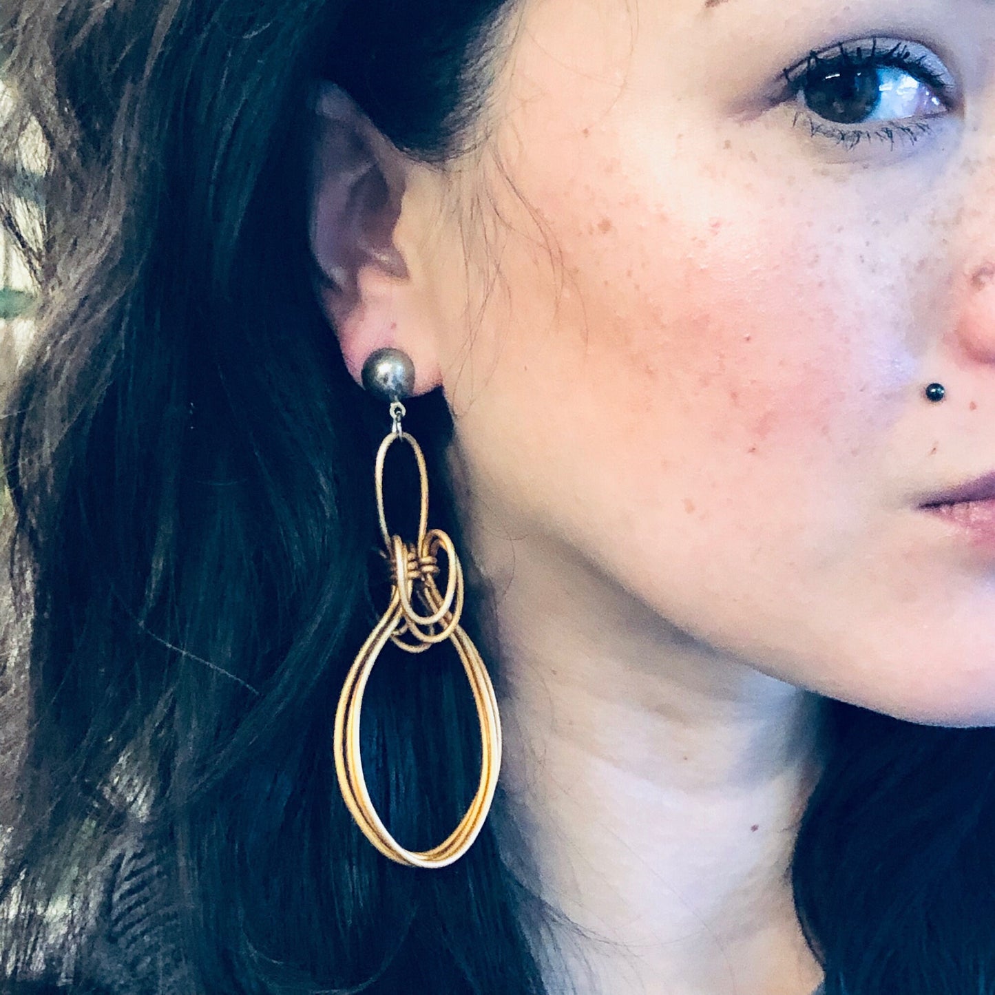 Close-up of a young woman's face with blue eyes wearing large, abstract gold wire dangle earrings