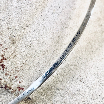 Close-up view of a sterling silver curved choker necklace on a light textured background