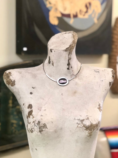 Vintage silver choker necklace with purple tiger's eye pendant on aged white mannequin torso in front of colorful artwork in background