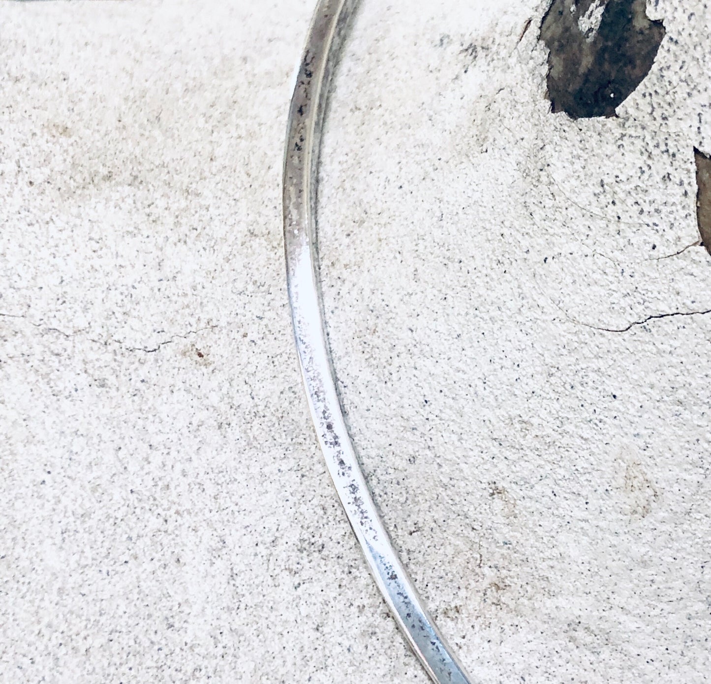 Curved metal silver choker necklace on rough white cement surface