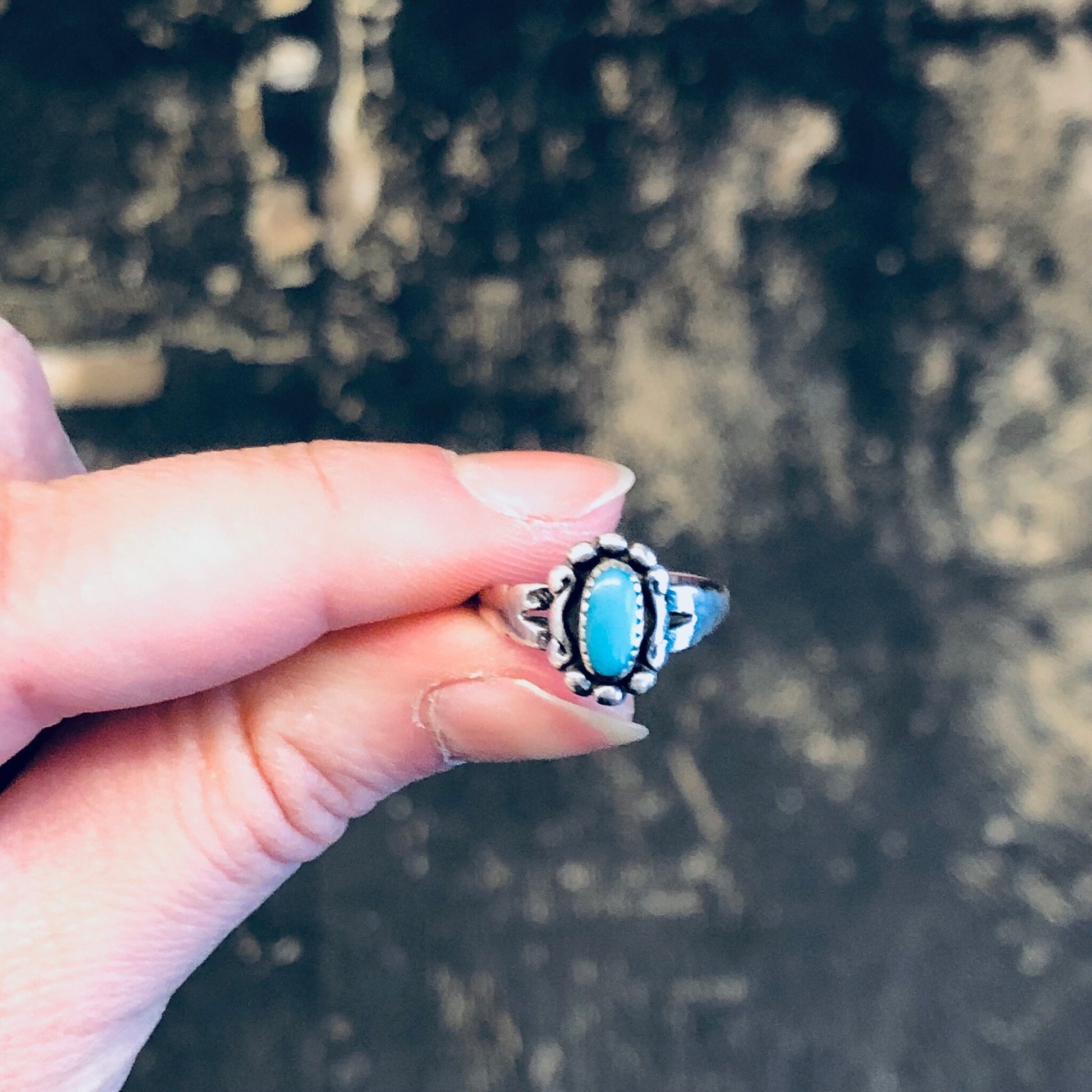 Vintage silver turquoise ring held between fingers, with blurred natural background