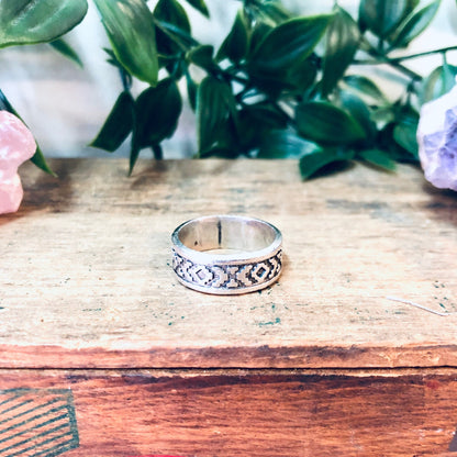 Vintage silver band ring with unique design on wooden surface next to colorful gemstones and green plant leaves, bohemian style jewelry gift idea for mom