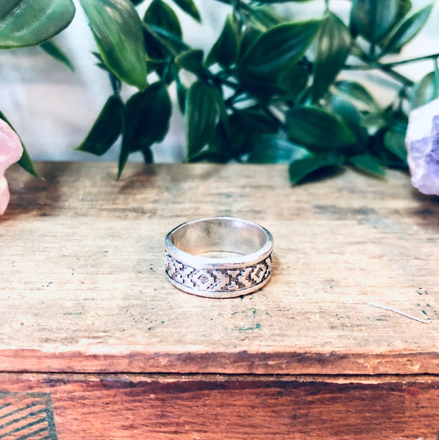 Vintage silver band ring with unique pattern design on wooden surface with plant in background